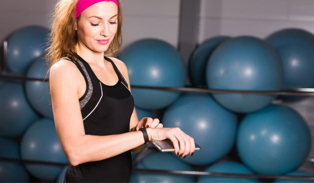 Attractive woman using cell phone and fitness tracker in gym