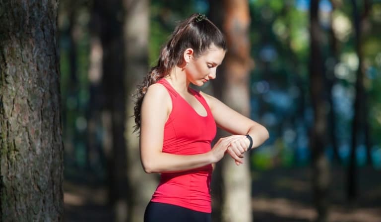 Beautiful woman runner looks at her fitness tracker getting ready for a run in the summer forest