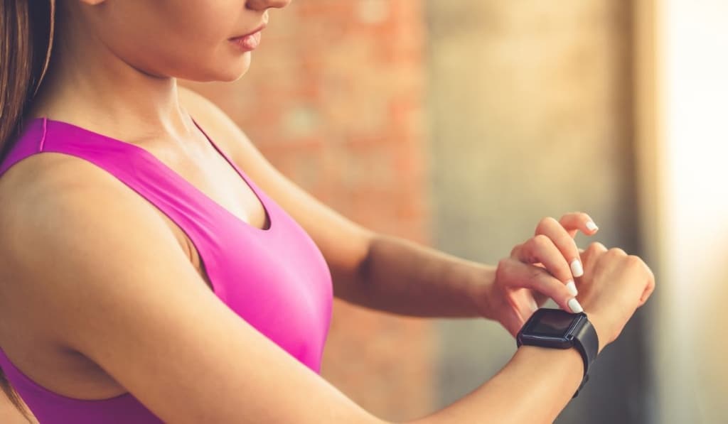 Cropped image of beautiful sports girl is switching on her fitbit before training while standing in fitness hall 
