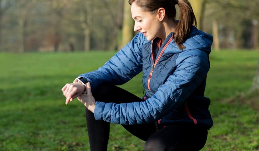 Woman Exercising In Winter Park Looking At Activity Tracker On Smart Watch 