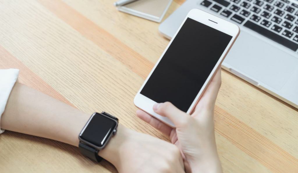 Woman holding a blank screen phone and a laptop and put a smart watch 