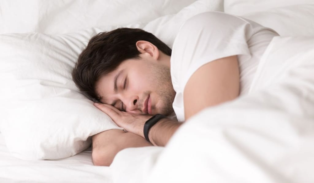 Young guy sleeping in bed wearing smartwatch or sleep tracker