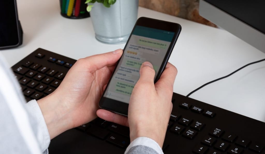 Close-up of female hands using modern smart phone while working at office with computer 