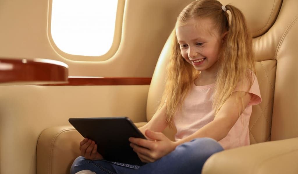 Cute little girl using tablet in airplane during flight